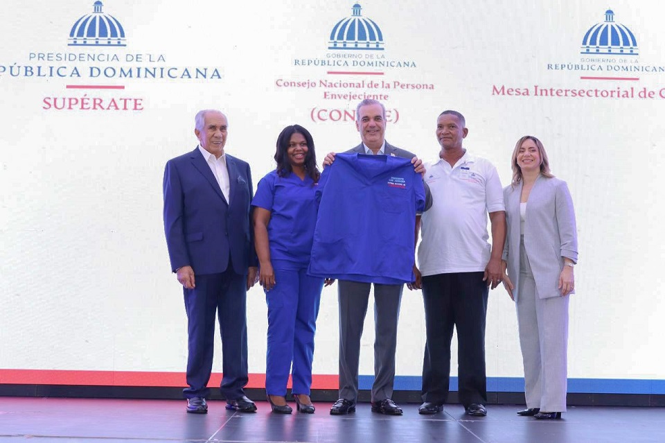 El presidente Luis Abinader recibe el uniforme simbólico de cuidador le acompañan el director ejecutivo de Conape, la directora general de Supérate y dos personas cuidadoras